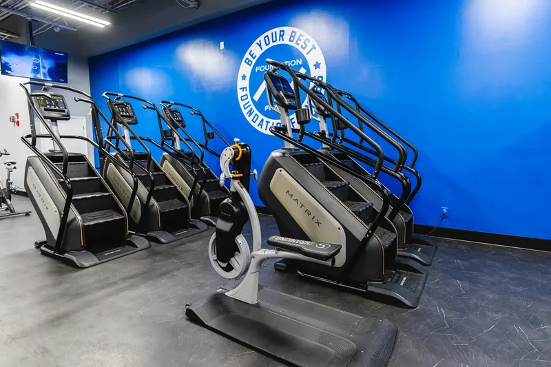 Stair climbers in front of the blue Be Your Best wall crest at Foundation Fitness Annapolis